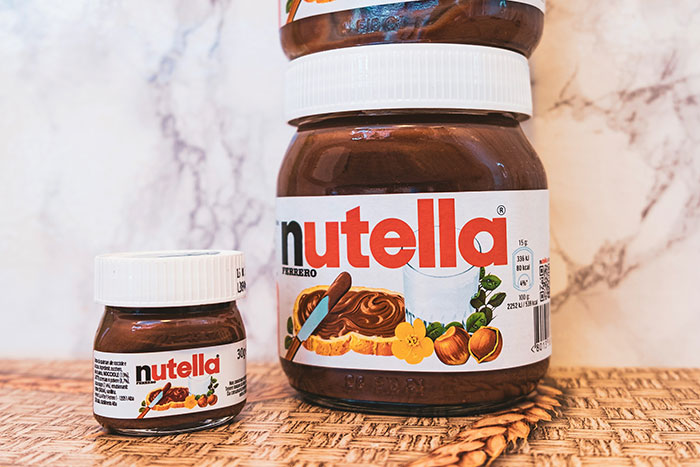 Nutella jars of different sizes on a wicker surface, representing product marketing and company sales strategies.