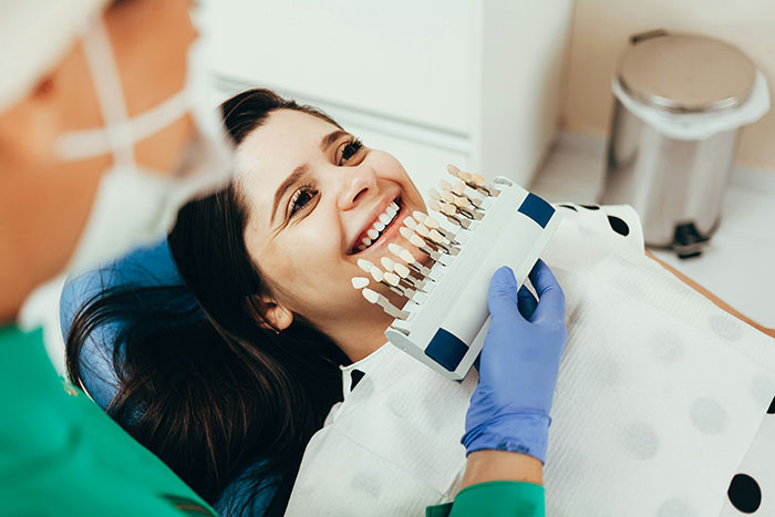 Dentist comparing tooth shades with a smiling patient, illustrating product marketing in dentistry.
