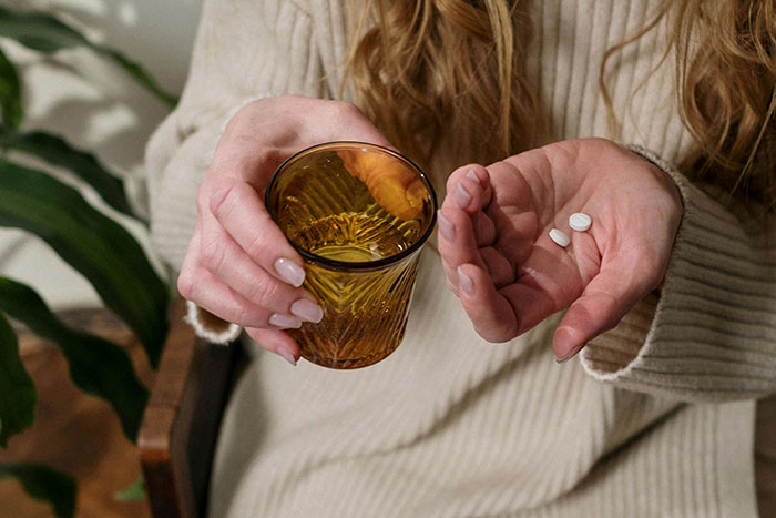 A person in a sweater holding a glass and pills, related to lies companies tell about products.