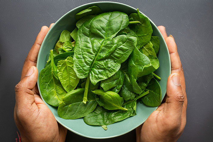 Hands holding a bowl of fresh spinach leaves, illustrating product sale misconceptions in marketing.