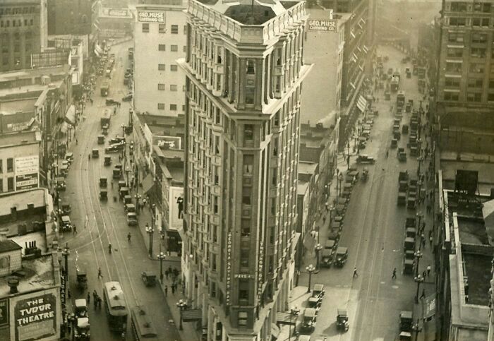 Aerial view of bustling American city streets with vintage cars and early 20th-century buildings showing life in America.