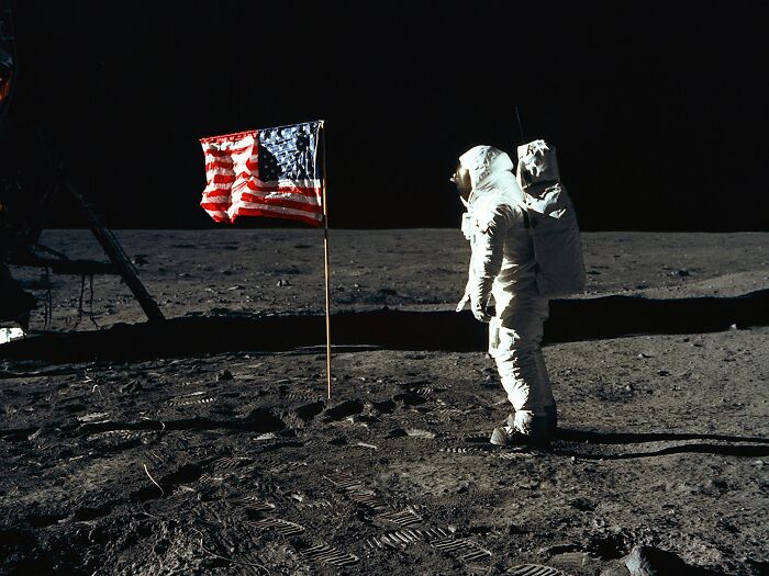 Astronaut confidently stands beside American flag on the moon's surface.