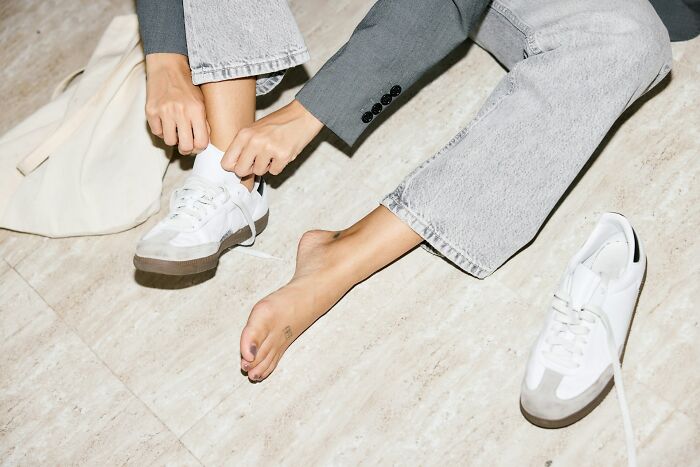 Person in denim sitting on floor tying shoelace, representing personal cleaning habits.