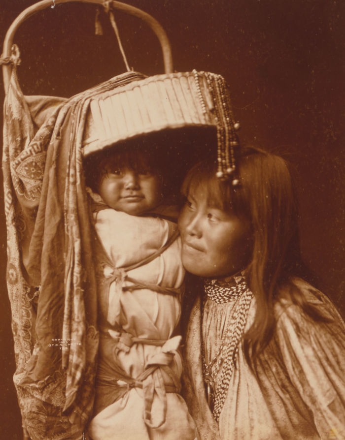 Native American woman with infant in traditional cradleboard, showcasing real lives from a century ago in haunting historic photo.