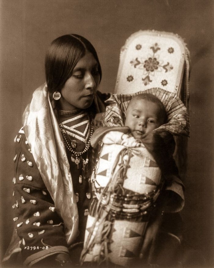 Native American woman holding a swaddled baby, showcasing real lives through haunting historical photography.