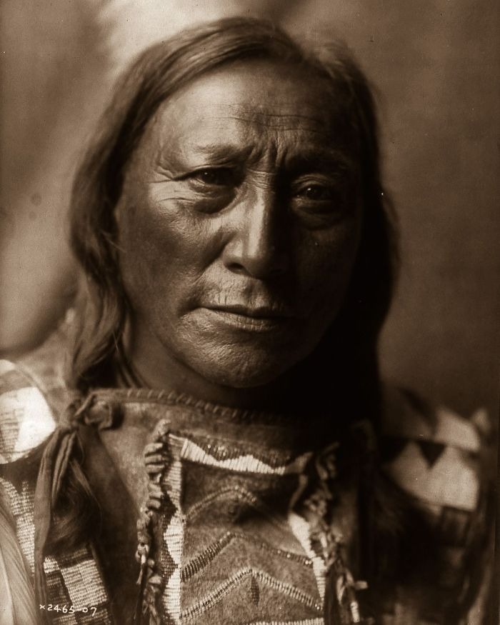 Portrait of a Native American man in traditional clothing capturing the real lives of Native Americans a century ago.