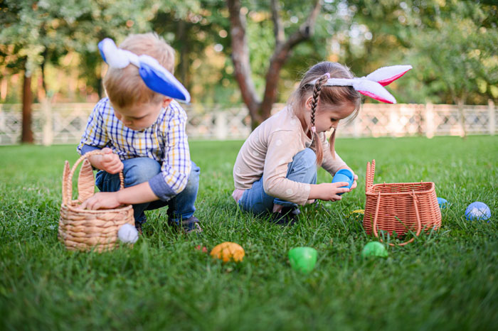 Two children with bunny ears on a grassy field collecting Easter eggs, highlighting a joyful Easter activity.