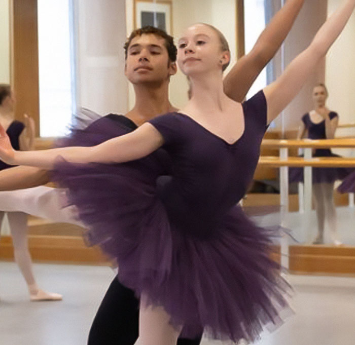Ballet dancers in a studio, wearing purple tutus, performing together, highlighting inclusion in ballet.