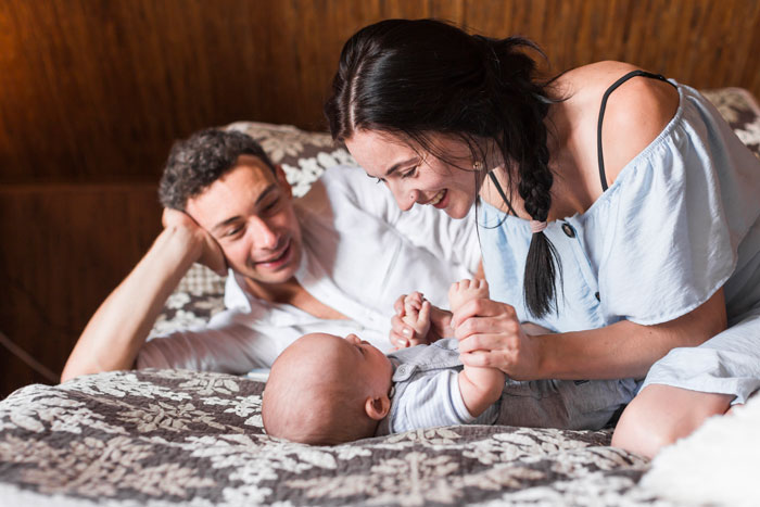 A couple enjoying a peaceful moment with their newborn in a cozy bedroom setting.
