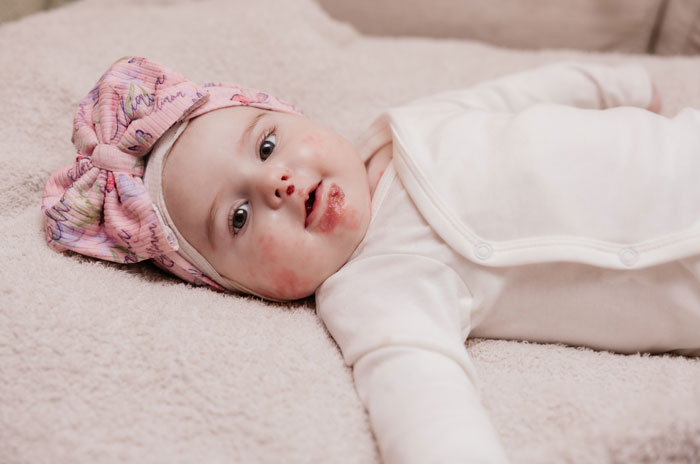 Baby girl in white outfit and pink headband lying down, related to influencer daughter's passing.