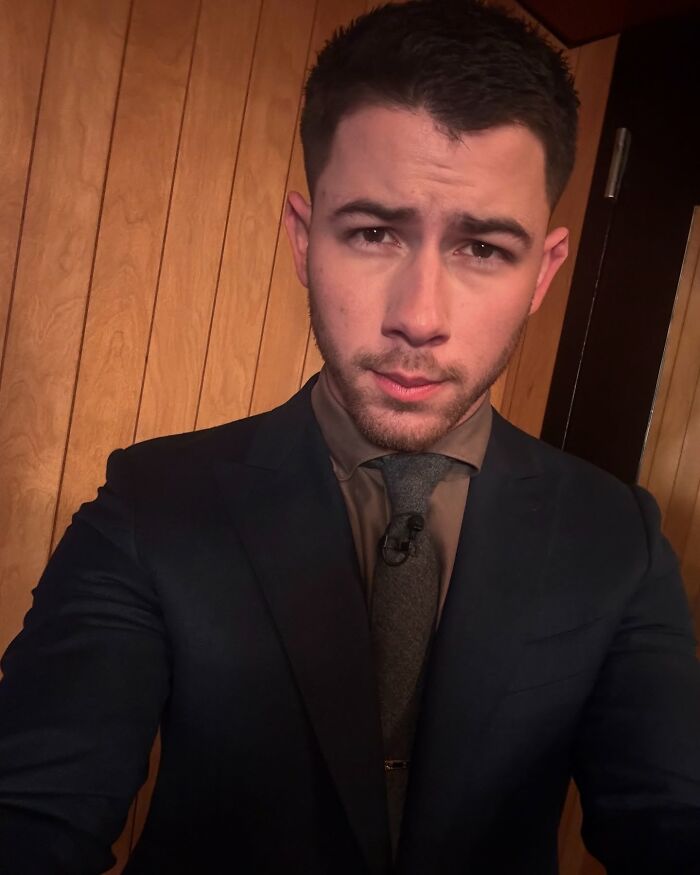 A celebrity in a suit taking a selfie against a wooden background.