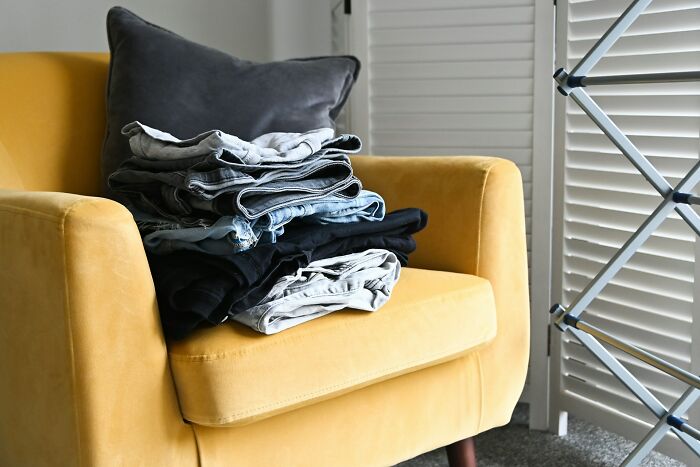 Folded clothes on a yellow chair next to a drying rack, reflecting personal cleaning rules.