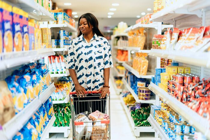 A woman shopping in a grocery aisle filled with snacks and canned goods.