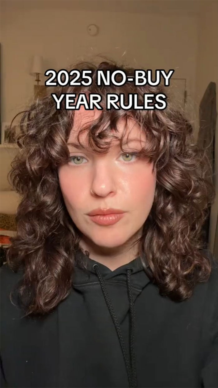 Person discussing No-Buy 2025 rules with curly hair and a black hoodie, emphasizing reduced consumerism.