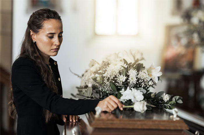 Woman at a funeral, contemplating a casket with flowers, reflecting on relationship and loss.