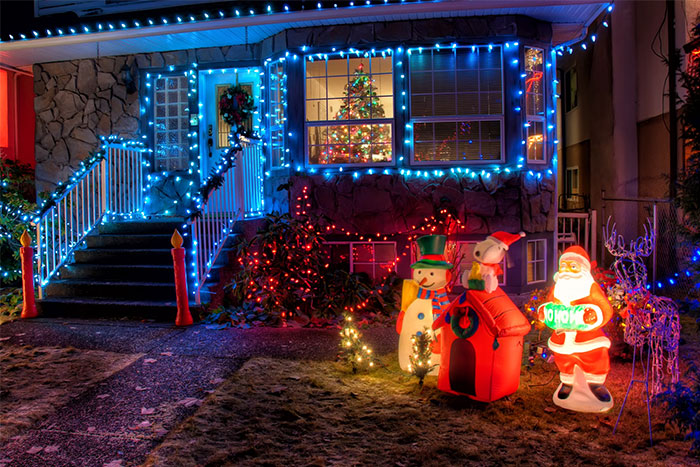 Festive US culture Christmas decorations with lights, inflatable figures, and a decorated tree visible through a window.