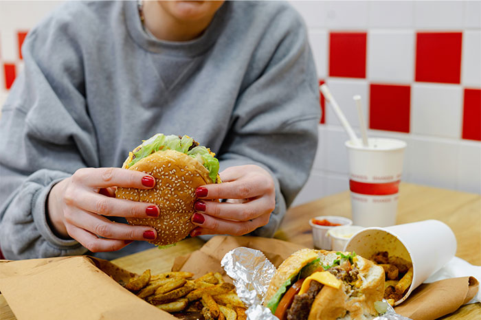 Person holding a burger with fries and a drink on the table, showcasing iconic US culture and fast food.