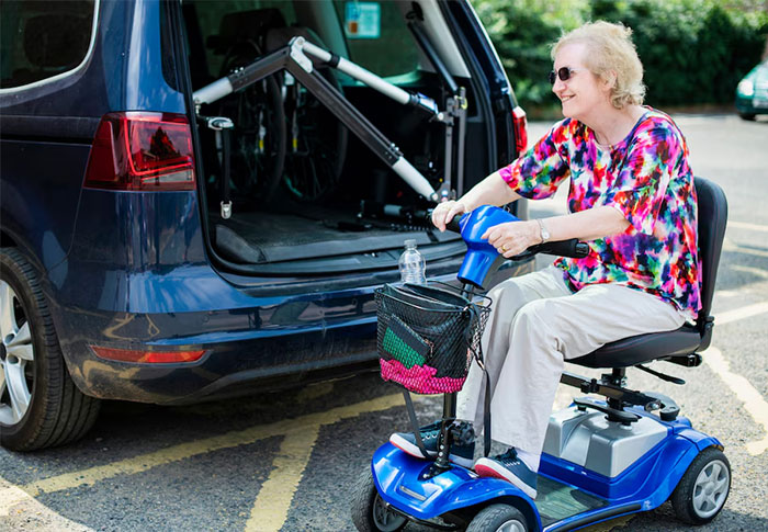 Woman on mobility scooter parking near car using a lift, illustrating nuances about US culture and travel experiences.