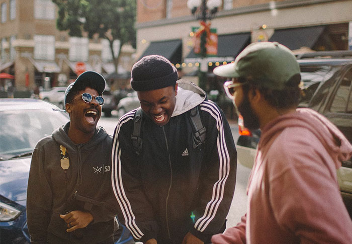 Three friends laughing together outdoors, showcasing casual style and US culture nuances in an urban setting.