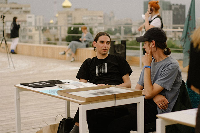 Two young men sitting and talking at an outdoor table showing nuances of US culture for travelers.