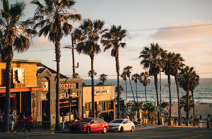 Sunset view of a California beach street with palm trees, shops, and cars, capturing US culture and travel nuances.