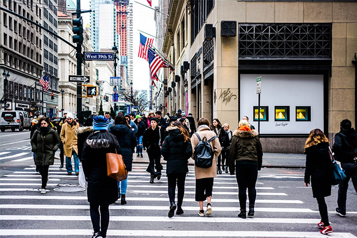 Busy city street scene with pedestrians crossing, American flags displayed, illustrating US culture nuances in urban travel.