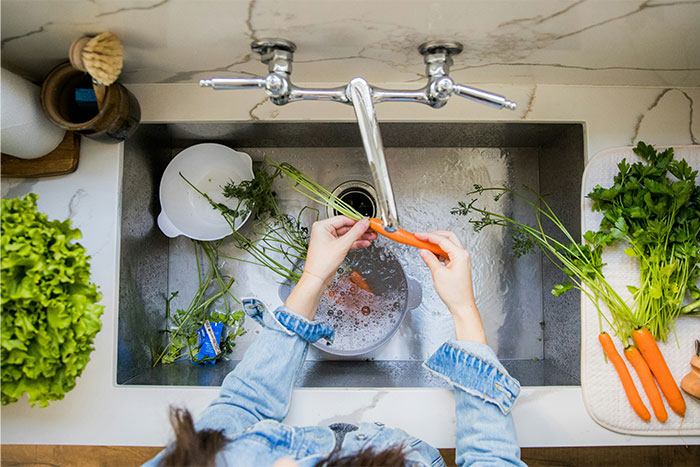 Person washing fresh vegetables in kitchen sink, showcasing US culture nuances in daily food preparation.