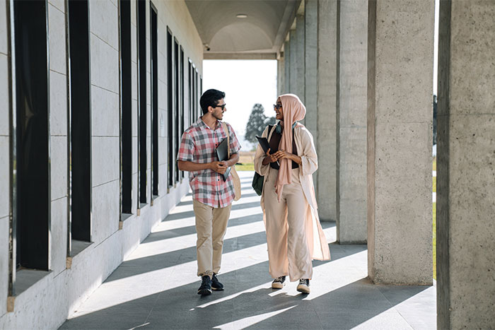 Two young travelers walking and chatting under a covered walkway, exploring nuances of US culture.