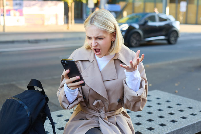 Woman on a street bench looking shocked at her phone, relating to a story about a group photo incident. Woman on a street bench looking shocked at her phone, relating to a story about a group photo incident.