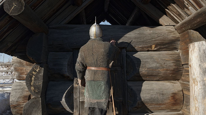 A medieval warrior in chainmail stands by a wooden cabin, evoking times when love potions were common.