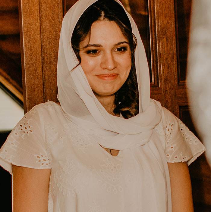 Woman in a white dress and veil, reminiscent of medieval times, standing indoors.