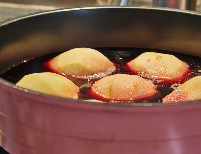 Peach halves simmering in red liquid, resembling a medieval-style love potion brewing in a pot.