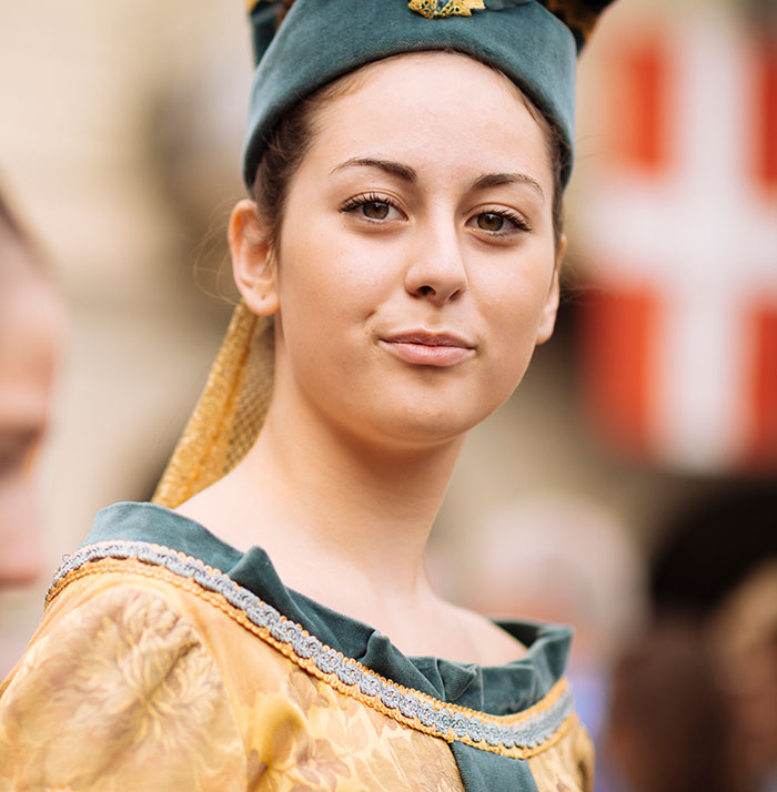 Young woman in medieval attire, wearing a green headdress, embodies normal medieval fashion in a historic setting.