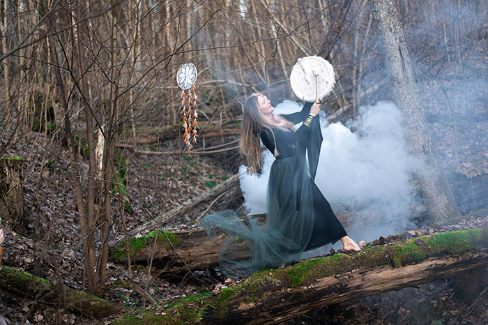 A woman in a forest performs a ritual with a drum and smoke, representing medieval love potions practices.