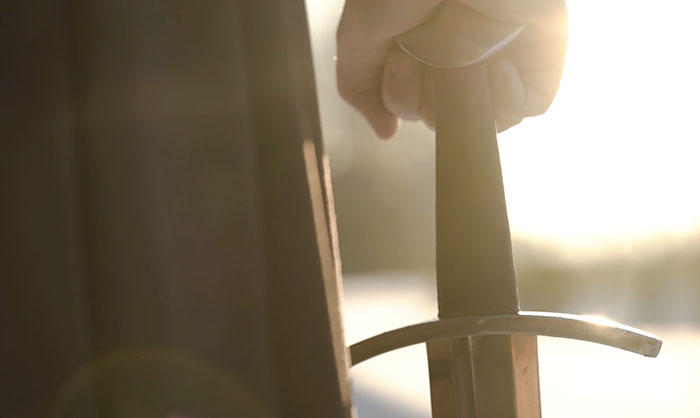 Hand holding a medieval sword, symbolizing historical customs contrasted with modern views.