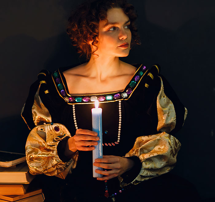 Woman in medieval attire holding a lit blue candle, reminiscent of love potion rituals from the past.