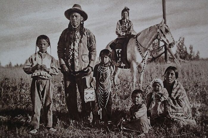 Native American family from a century ago dressed in traditional clothing in an outdoor field setting.