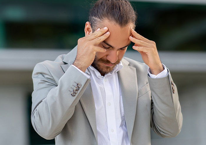 Man in a beige suit, looking troubled, hands on forehead, representing a dilemma about his female best friend and child's birth.