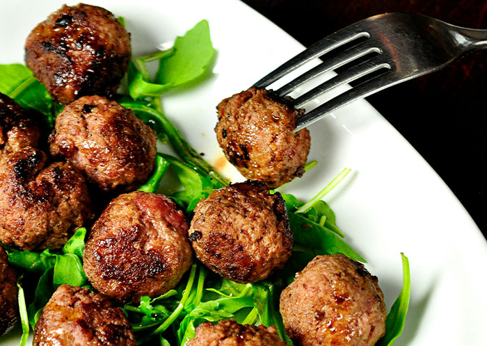 Vegetarian meatballs served on a bed of greens with a fork picking up one meatball.