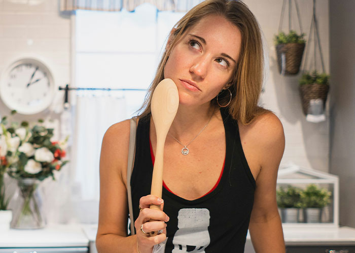 Woman in a kitchen pondering with a wooden spoon, relating to vegetarian meatballs incident.
