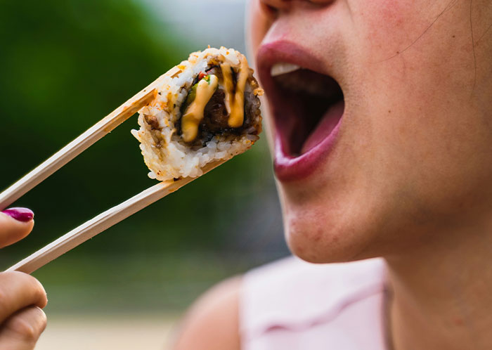 Person eating sushi with chopsticks, highlighting vegetarian meal experience.