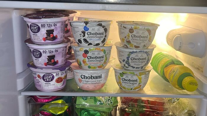Open refrigerator shelf filled with various Greek yogurts, illustrating a funny relationship argument over food choices.