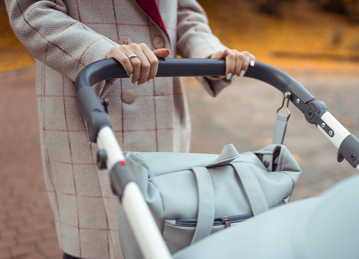New mom pushing a stroller outdoors, wearing a plaid coat and rings, representing teen pregnancy theme. New mom pushing a stroller outdoors, wearing a plaid coat and rings, representing teen pregnancy theme.