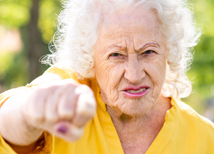 Elderly woman in yellow shirt, looking angry and pointing, outside. Elderly woman in yellow shirt, looking angry and pointing, outside.