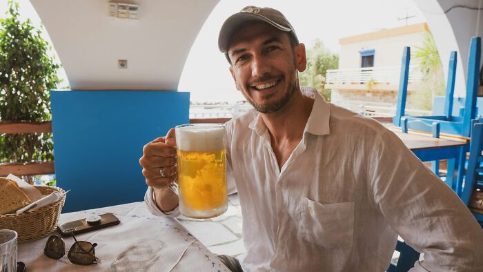 Man smiling and holding a glass of beer in a relaxed setting, enjoying a super normal thing country experience.