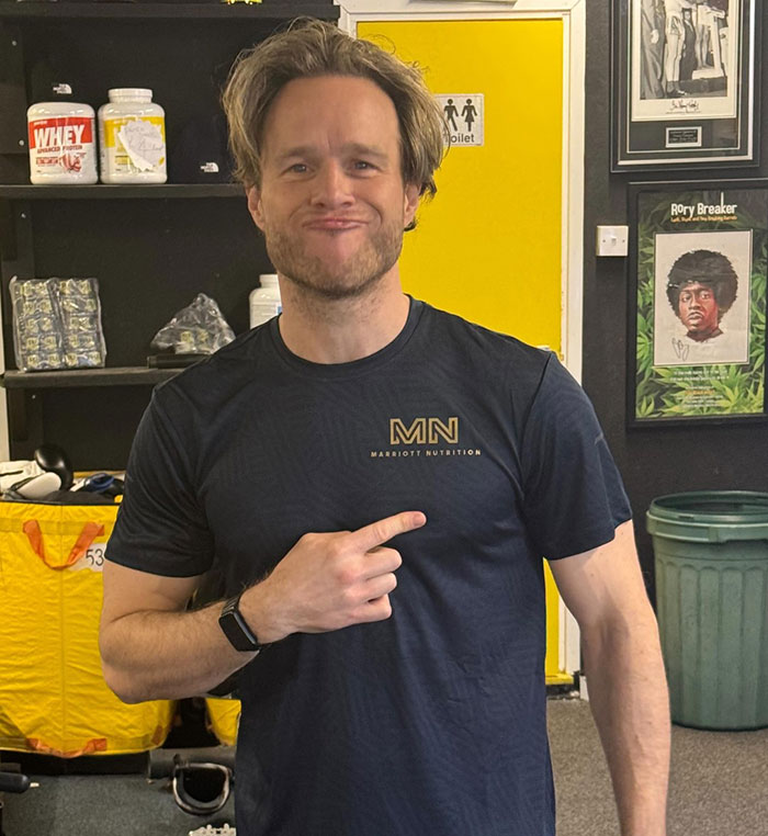 Singer in a gym pointing at his physique transformation, sparking a heated debate between men and women.