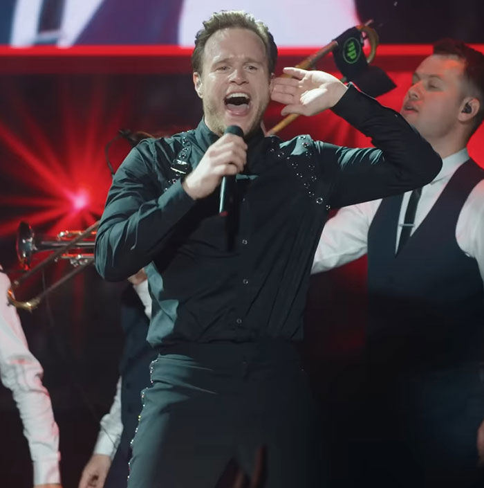 Singer performing on stage in black outfit, highlighting physique transformation that sparked debate between men and women.