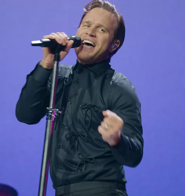 Singer performing on stage with microphone, showcasing physique transformation sparking debate between men and women.