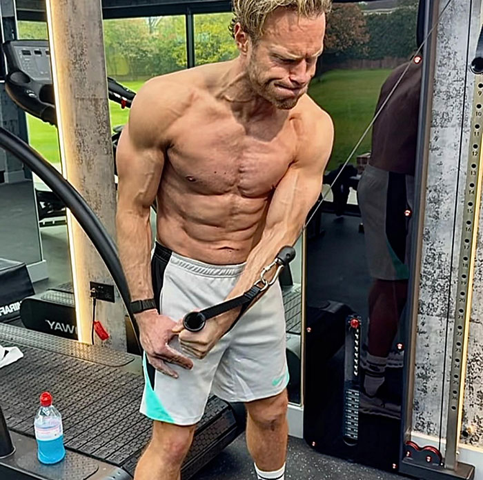 Muscular singer showing physique transformation while working out with cable machine in a gym setting.