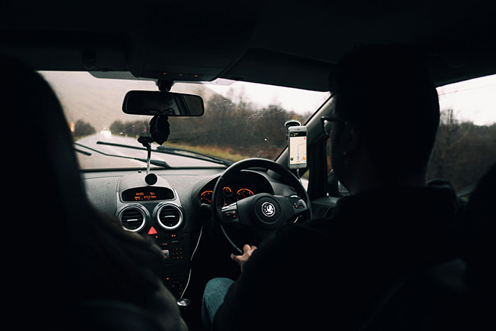 Man driving on a road trip, possibly visiting a long-distance girlfriend, with a GPS visible on the dashboard.